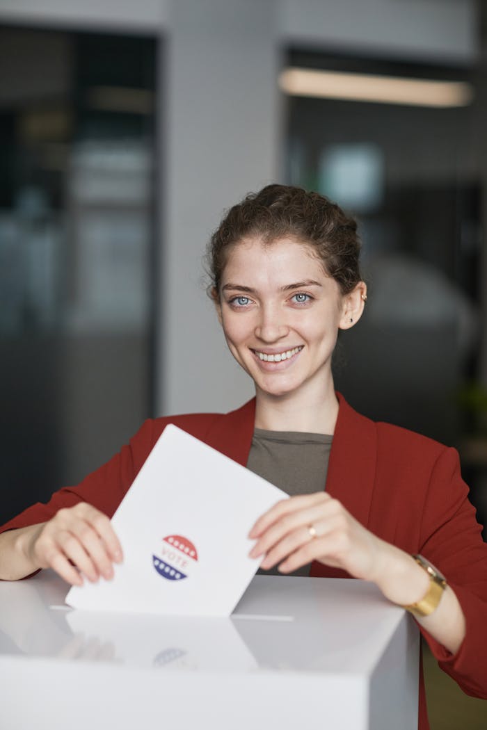 Smiling woman in red blazer casting her vote during election day in a modern indoor setting.